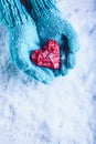 Woman hands in light teal knitted mittens are holding beautiful entwined vintage red heart in a snow. St. Valentine concept. Royalty Free Stock Photo