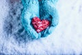 Woman hands in light teal knitted mittens are holding beautiful entwined vintage red heart in a snow. St. Valentine concept. Royalty Free Stock Photo