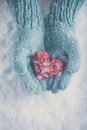 Woman hands in light teal knitted mittens are holding beautiful glossy red heart on snow background. Love, St. Valentine concept