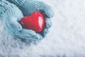 Woman hands in light teal knitted mittens are holding beautiful glossy red heart in snow background. Love, St. Valentine concept Royalty Free Stock Photo