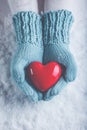 Woman hands in light teal knitted mittens are holding beautiful glossy red heart in snow background. Love, St. Valentine concept Royalty Free Stock Photo
