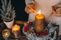 Woman hands lightning big gold candle with matches in Christmas wreath. Xmas interior decoration on rustic wooden background.hygge Royalty Free Stock Photo