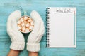 Woman hands in mittens hold cup of hot cocoa or chocolate with marshmallow and notebook with wish list on turquoise vintage