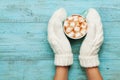 Woman hands in mittens hold cup of hot cocoa or chocolate with marshmallow on turquoise vintage table from above. Flat lay style. Royalty Free Stock Photo