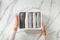 Woman hands neatly folding underwears and sorting in drawer organizers on white marble background.