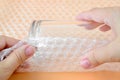 Woman hands packaging a glass for water with white transparent bubble wrap on a yellow background. Material for packing fragile