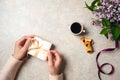 Woman hands packing gift box over feminine desk decorated with coffee cup, cookies, lilac flowers and purple ribbon. Flat lay, top