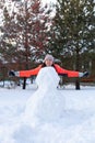 Woman with hands parallel to ground covered with snow, carrot in mouth standing behind incomplete snowman in evening Royalty Free Stock Photo