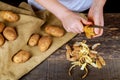 Woman hands peel potato, peelings on wooden cutting board. Three clean potatoes on plate.