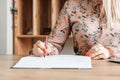 Woman hands with pencil, she is is writing in her notebook sitting at the table with book shelf background. Copy, empty space for Royalty Free Stock Photo