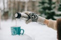 Woman hands pours hot tea or coffee out of thermos on winter forest background. girl using a thermos in on a snowy mountain. red Royalty Free Stock Photo