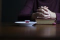 Woman hands in prayer posture on top of open bible with eucharist sacraments on top of table