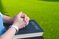 Woman hands praying on Holy Bible while sitting on green lawn in front yard area Royalty Free Stock Photo