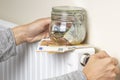 Woman hands put glass savings jar with cash money and adjusting temperature of central heating radiator at home. Family Royalty Free Stock Photo