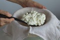 Woman hands putting mess of fermented cheese or cottage cheese or greek yogurt on the waffle towel using skimmer