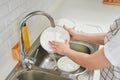 Woman hands rinsing dishes under running water in the sink