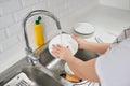 Woman hands rinsing dishes under running water in the sink