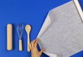 Woman hands roll baking paper. Wooden spoon, rolling pin and balloon whisk on blue background. Top view