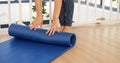 Woman hands rolled up yoga mat on gym floor in yoga fitness training room. Home workout woman close up hands rolling foam yoga gym