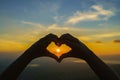 Woman hands silhouette on beautiful sunset above the mountain in the form of love heart-shaped hand gesture Concept of love, life Royalty Free Stock Photo