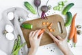 Woman hands slicing carrots on wooden cutting board, surrounded with vegetables. Flat lay, top view Royalty Free Stock Photo