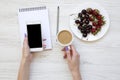 Woman hands with smartphone, latte, notebook, strawberries and cherries on white wooden background, top view. Royalty Free Stock Photo