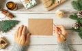 Woman hands in sweater writing on blank envelop greeting card . Flat lay of white wooden background with eco natural