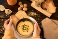 Woman hands touching a bowl of pumpkin soup served with bread croutons and pumpkin seeds. Wooden background Royalty Free Stock Photo