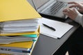 Woman hands typing on laptop computer with binders filled with papers in foreground. Selective focus Royalty Free Stock Photo