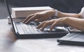 Woman hands typing on laptop keyboard with books and various devices on wooden table Royalty Free Stock Photo