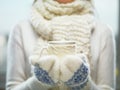 Woman hands in white and blue mittens holding a cozy knitted cup with hot cocoa, tea or coffee. Winter and Christmas time concept.