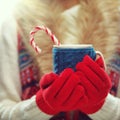 Woman hands in woolen red gloves holding cozy mug with hot cocoa, tea or coffee and candy cane. Winter and Christmas time concept. Royalty Free Stock Photo