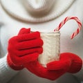 Woman hands in woolen red gloves holding a cozy mug with hot cocoa, tea or coffee and a candy cane. Royalty Free Stock Photo