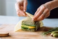 Woman hands wrapping a healthy sandwich in beeswax food wrap. Generative AI