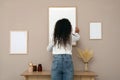 Woman hanging empty frame on pale rose wall over table in room, back view Royalty Free Stock Photo