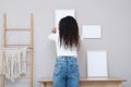 Woman hanging empty frame on pale rose wall over table in room, back view Royalty Free Stock Photo