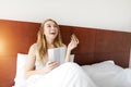 Woman happy with debit credit card and tablet laying in white bed at home with sunshine