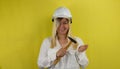 A woman in a hard hat with a hammer smiles slyly on a yellow background. A woman in a construction helmet holds a hammer Royalty Free Stock Photo