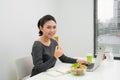 Woman has healthy business lunch in modern office interior. Young beautiful businesswoman at working place, eating vegetable Royalty Free Stock Photo