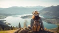 Woman with a hat and backpack looking at the mountains and lake from the top of a mountain in the sunlight, with a view of the Royalty Free Stock Photo