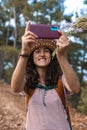 A woman in a hat and with a backpack walks along a forest path and takes a selfie