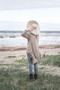 A woman in a hat and a long cardigan stands against the sea during a storm, rear view