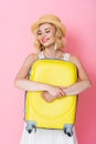 Woman in hat embracing yellow luggage