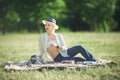 A woman in a hat is holding a glass of red wine in her hand at a picnic. Lady sitting on the grass with a blanket Royalty Free Stock Photo