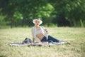 A woman in a hat is holding a glass of red wine in her hand at a picnic. Lady sitting on the grass with a blanket Royalty Free Stock Photo