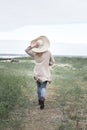 A woman in a hat and a long cardigan runs to the sea during a storm, rear view