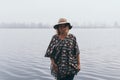 Woman in hat and poncho standing on the river bank and looking towards autumn forest covered with morning fog Royalty Free Stock Photo