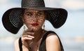 Woman in Hat Portrait. Fashion Luxury Model in Black Summer Hat with Make up and Golden Jewelry. Close up Beauty Face over Sky