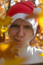 A woman in a hat of Santaclaus with a sly evil face among the autumn foliage as a harbinger of the coming winter.