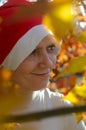 A woman in a hat of Santaclaus with a sly evil face among the autumn foliage as a harbinger of the coming winter.